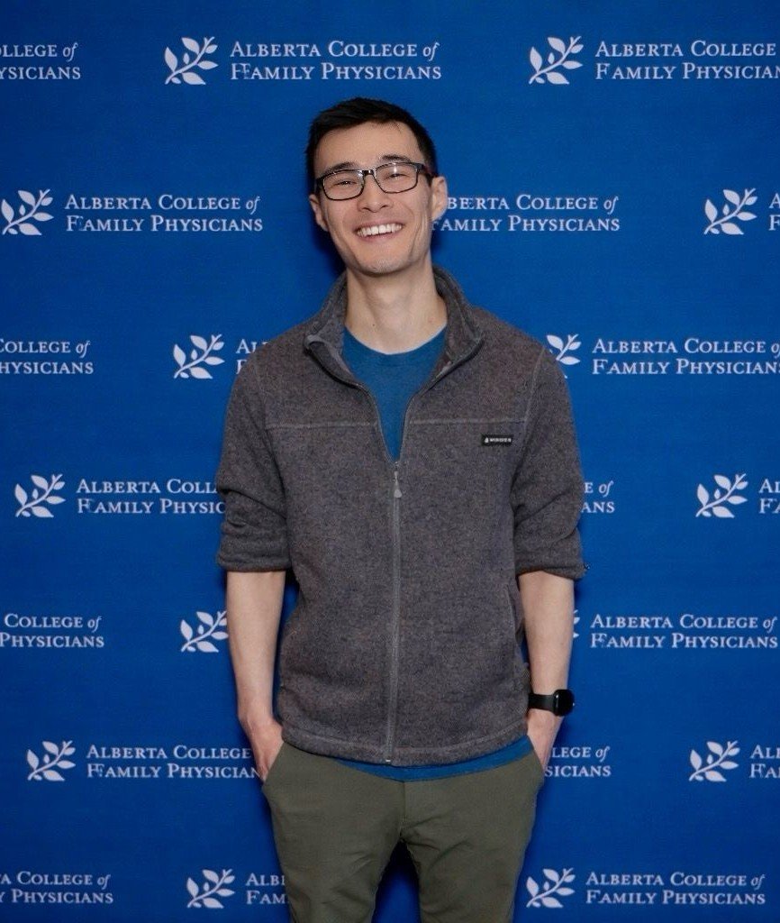Smiling man with glasses stands in front of a blue Alberta College of Family Physicians backdrop.